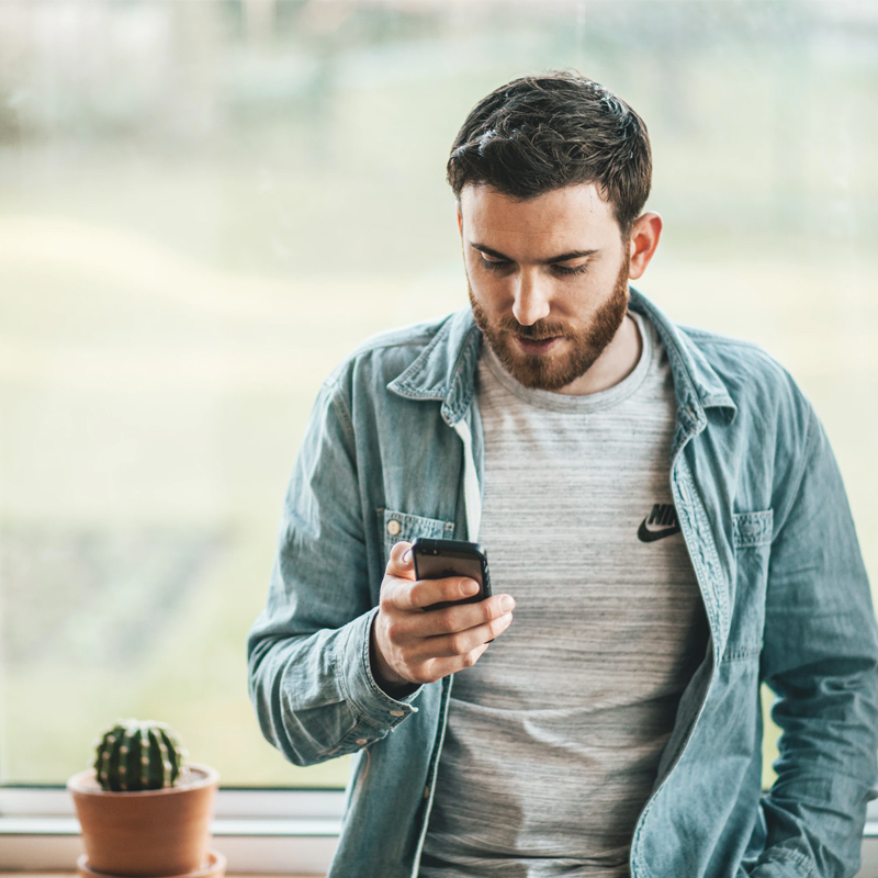 An image of a young man looking at his mobile phone to support article '5 Reasons Customers Prefer Live Chat (When It’s Done Well)'